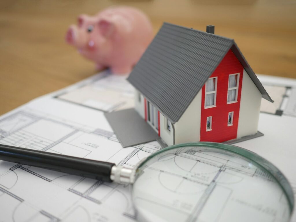Small model house beside a magnifying glass representing a closer look at real estate investing returns in 2026
