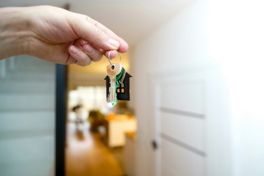 Hand holding a house key inside an empty home representing what happens after a foreclosure sale in 2026